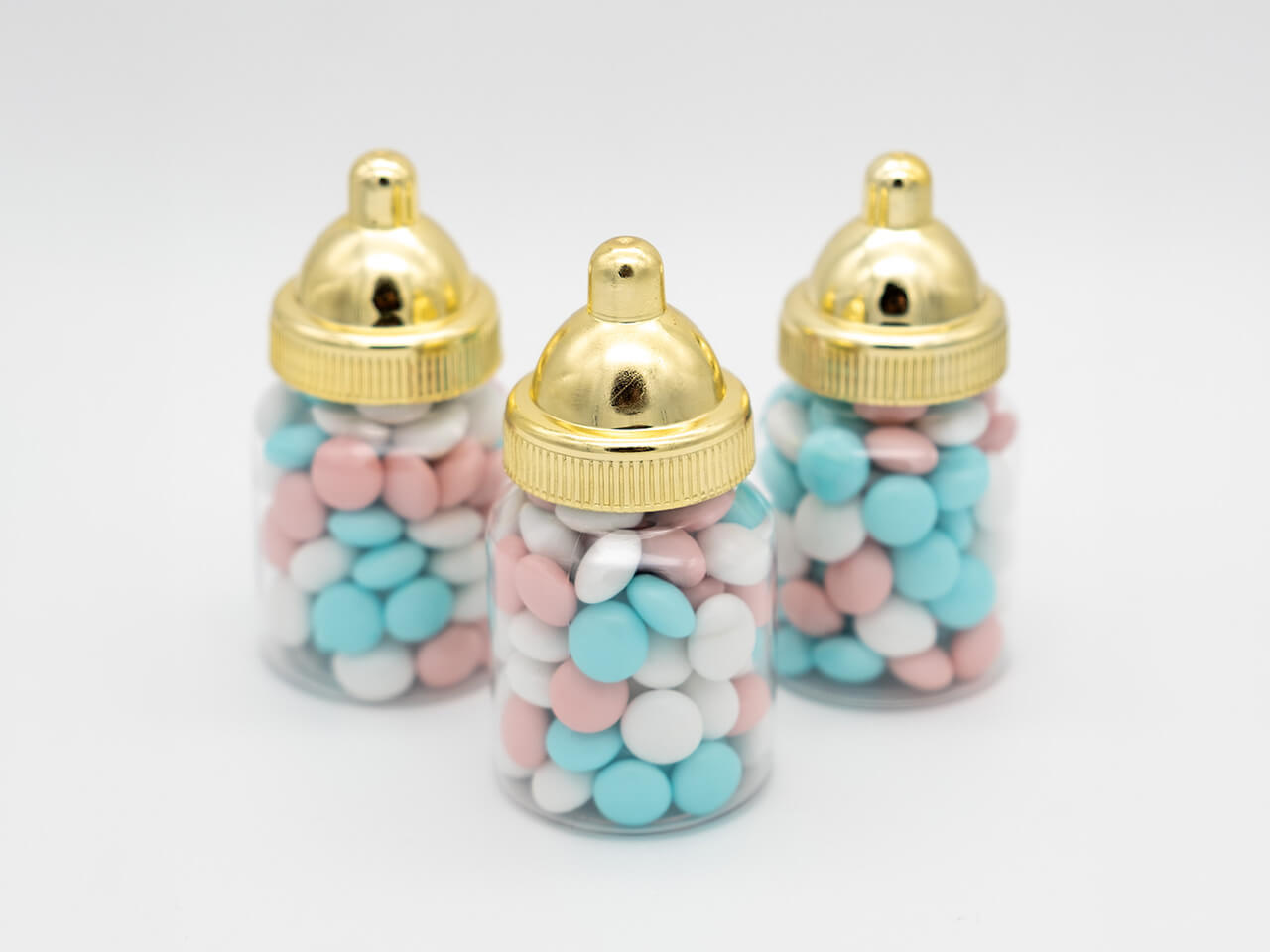 Drie babyflesjes met blauwe, roze en witte chocoladedragees en goudkleurige doppen
